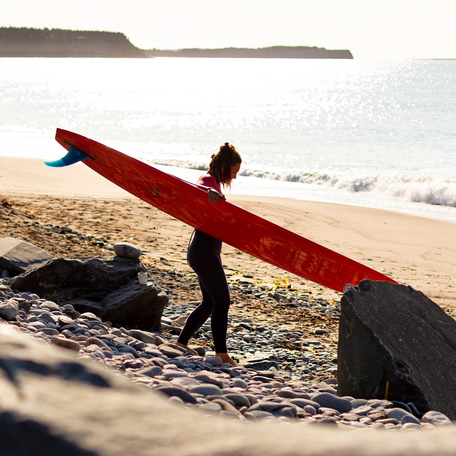 Person carrying a red surfboard on a beach with ocean waves in the background